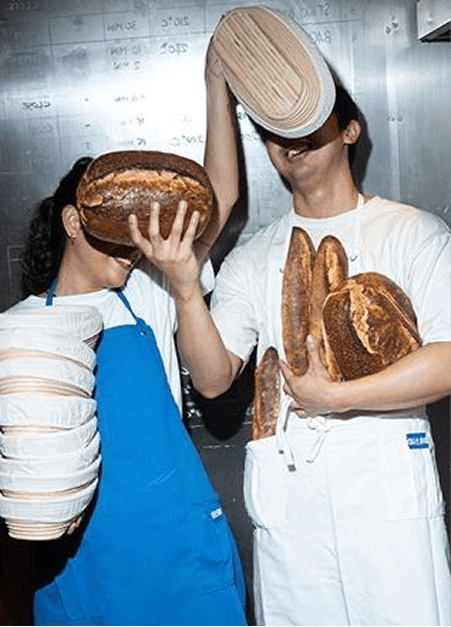 Two bakers playfully carrying loaves of bread
